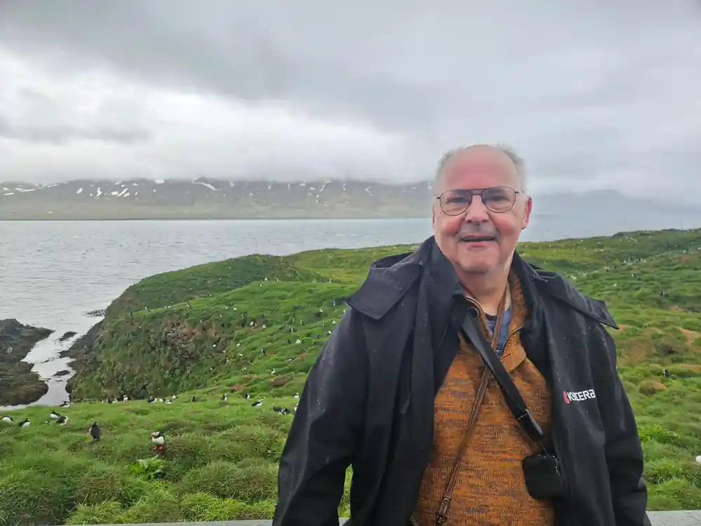 Man in glasses and jacket standing by coastal grassland