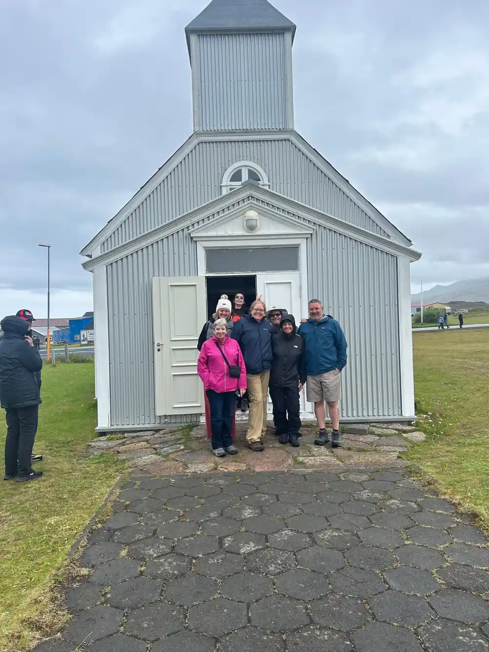 People standing outside small white corrugated metal church building