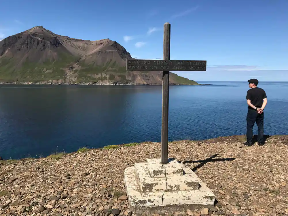 Stone cross on pebbly beach overlooking mountain and water