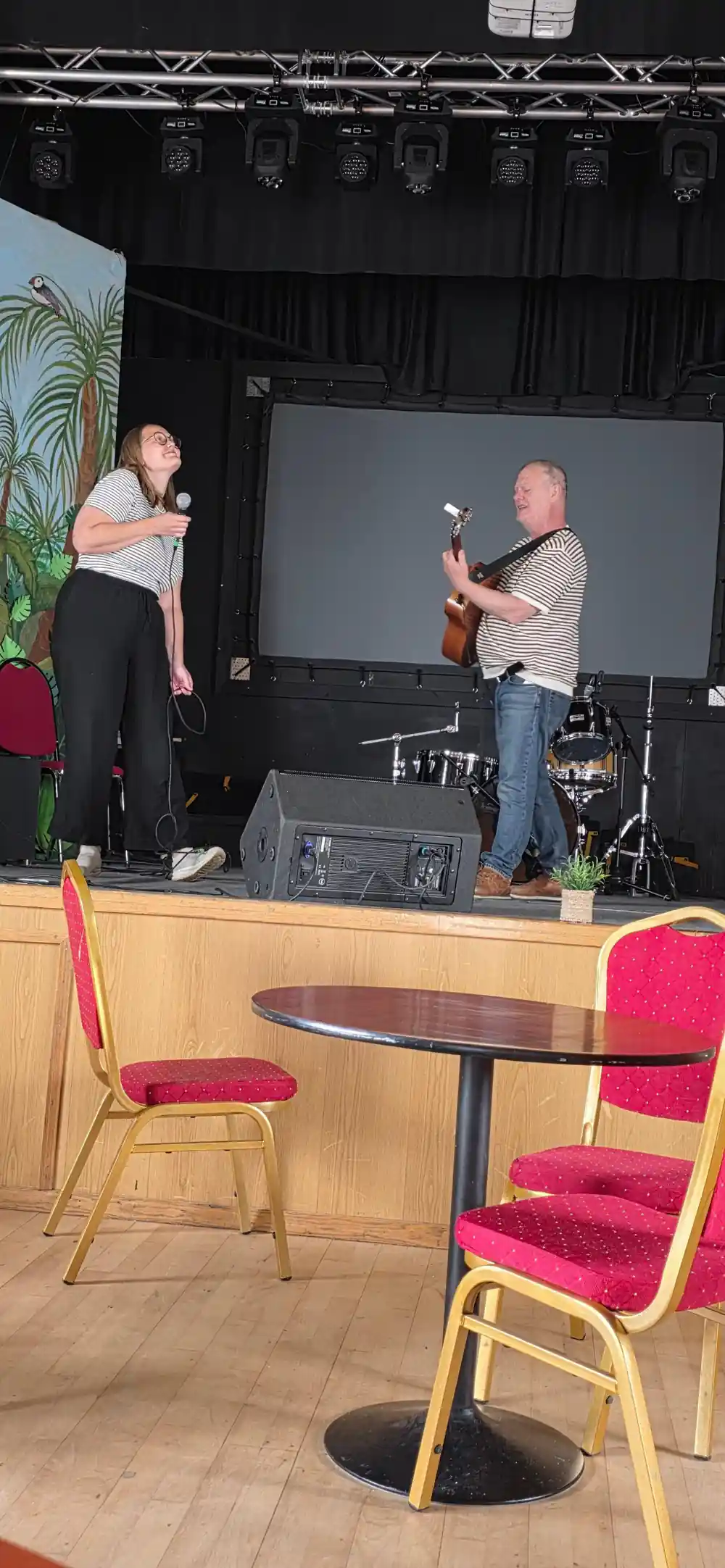 Two people on stage with microphones and screen