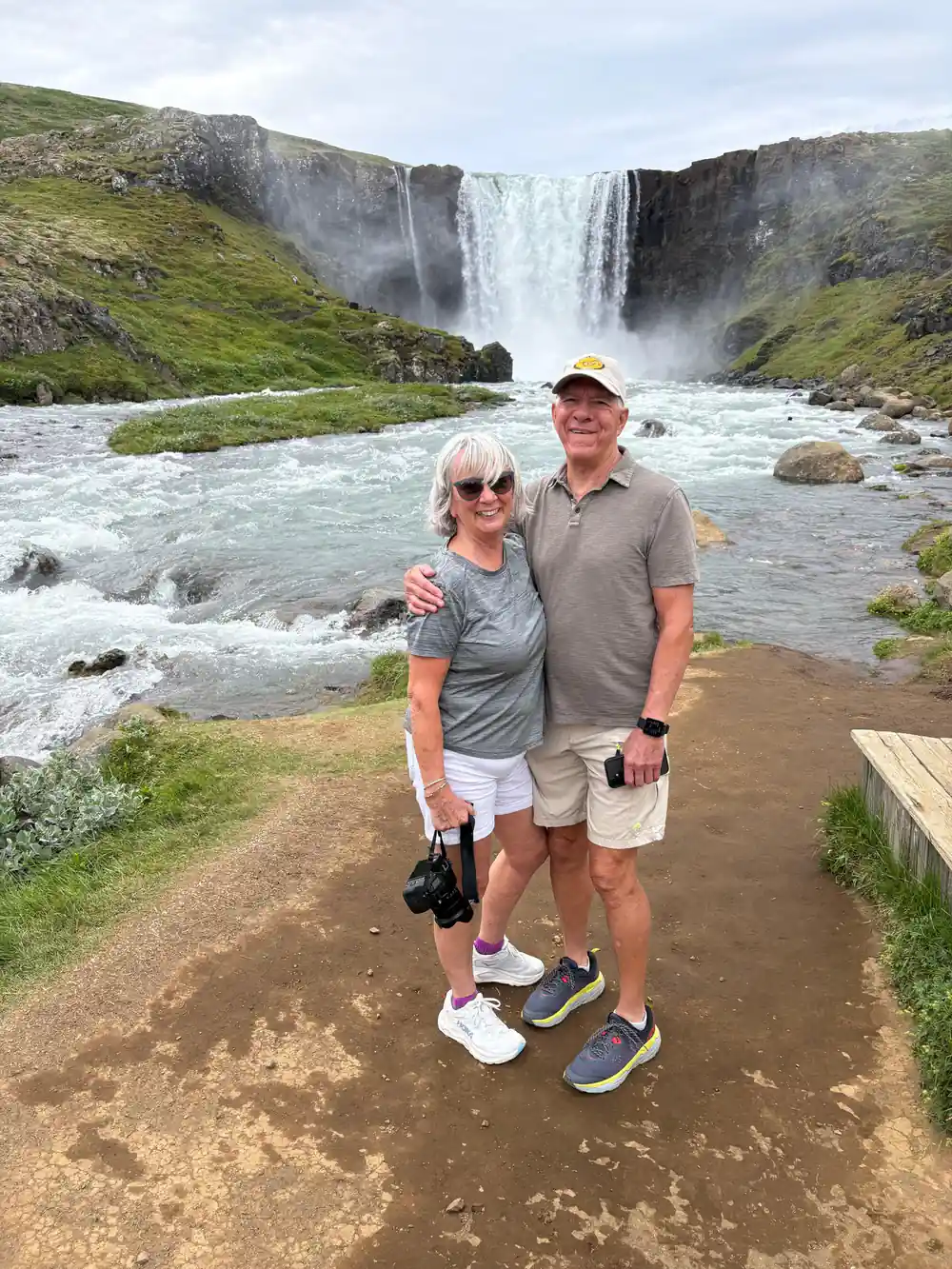Two people standing at waterfall with turquoise river and rock