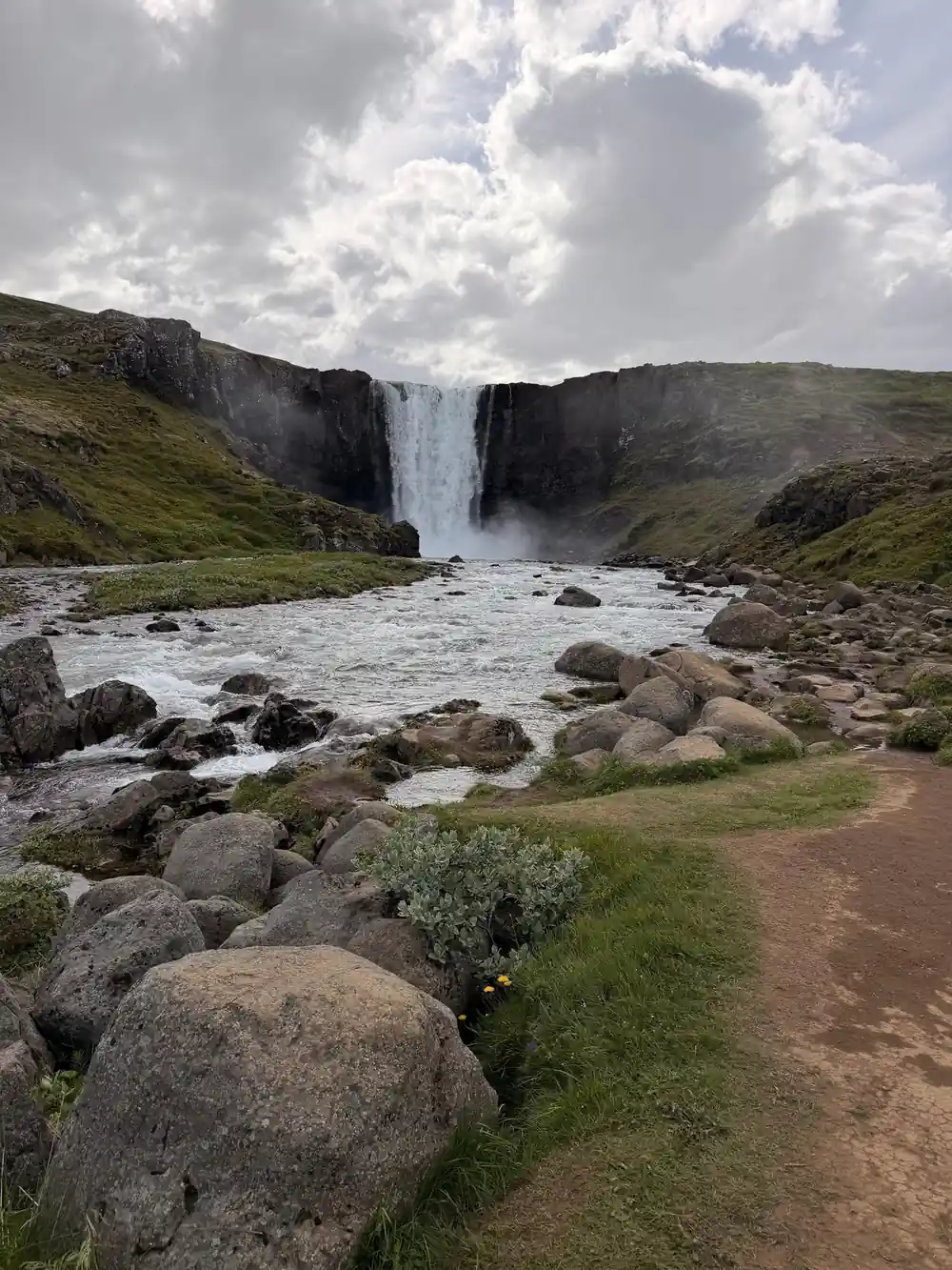 Waterfall dropping into river valley with green hillside
